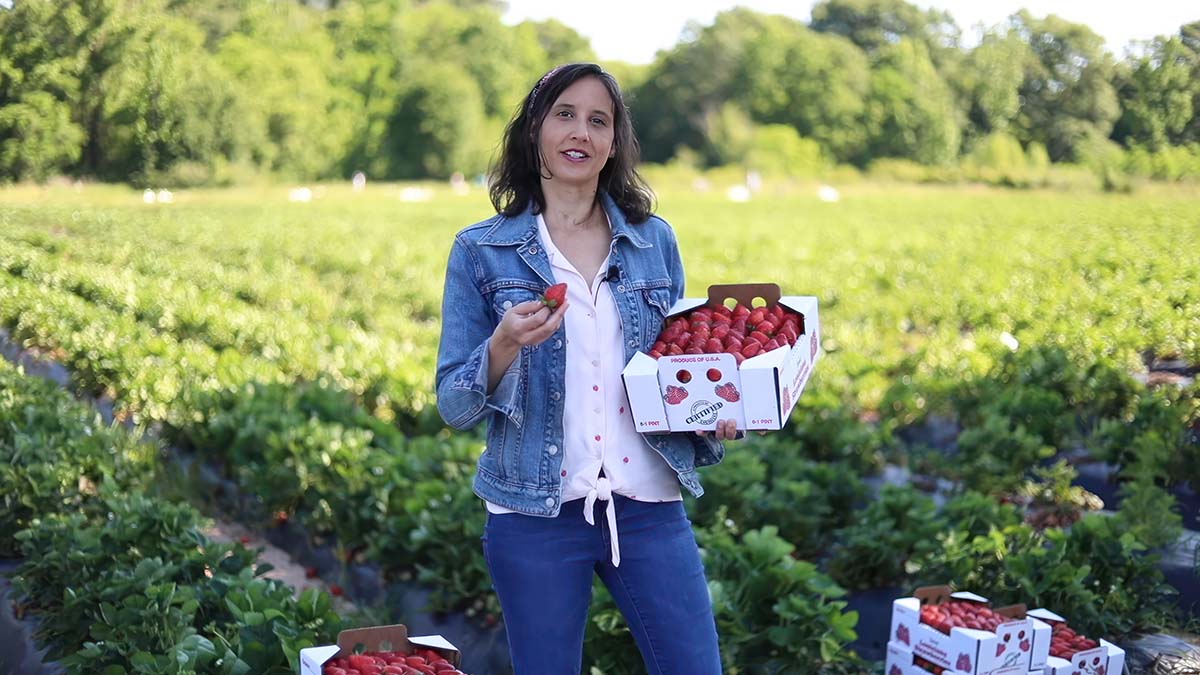 A woman holds a box of strawberries while standing in a field. 